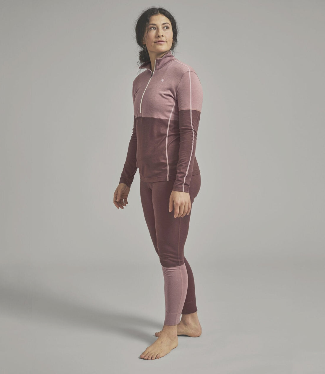 Woman wearing a two-tone purple and pink baselayer outfit on a gray background